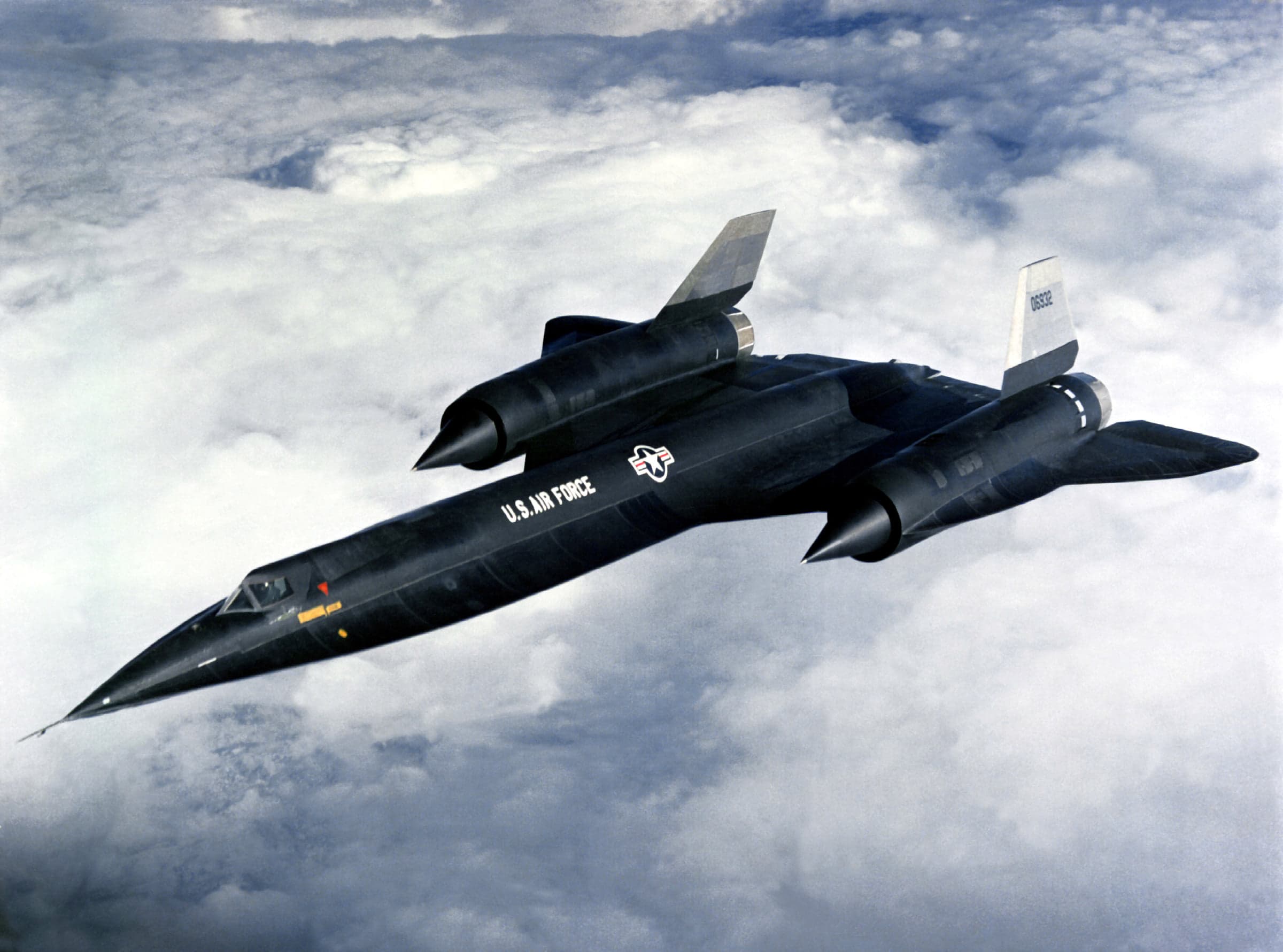 A black Lockheed A-12, serial 60-6932, in flight above clouds. One canopy; the forward chines run to the nose.